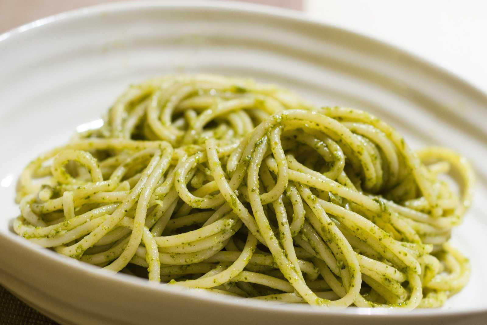 A bowl-shaped ceramic plate with pesto and pasta in it